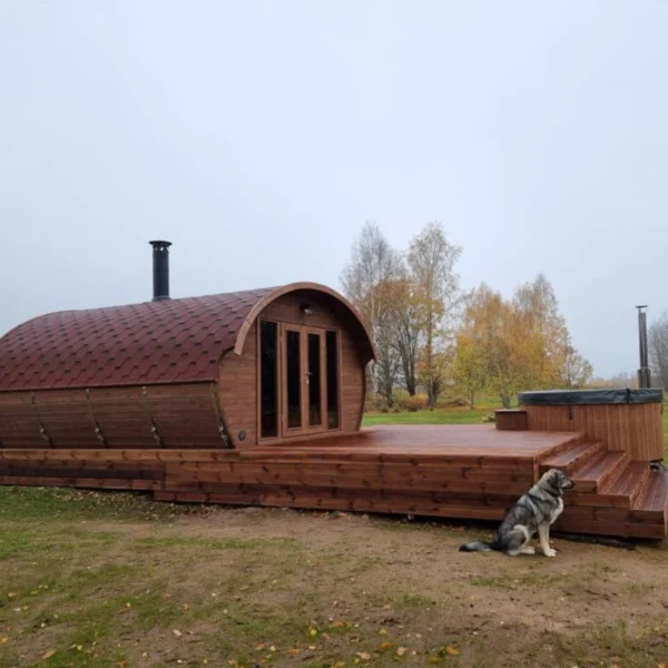 Ilmarinen sauna installed on a spacious wooden terrace, with its curved roof design, glass doors, and integrated chimney, blending seamlessly with the outdoor landscape.